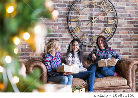 Young women surprising each other with Christmas gift while sitting on sofa in loft Young women surprising each other with Christmas gift while sitting on sofa in loft 109951150