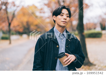 コーヒーを飲みながら紅葉の並木道を歩く男性 109951542