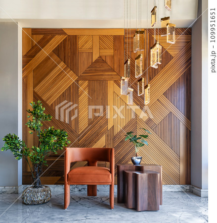 Modern orange chair and coffee table against wood wall with lights and potted plant Modern orange chair and coffee table against wood wall with lights and potted plant 109951651