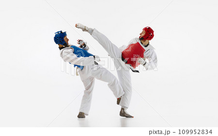 Two men in kimono and helmets practicing taekwondo, training, fighting isolated over white background. Martial arts, combat sport Two men in kimono and helmets practicing taekwondo, training, fighting isolated over white background. Martial arts, combat sport 109952834