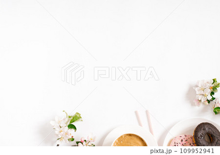 Morning breakfast of a freelance blogger. A cup of coffee with sweet donuts and white apple blossoms in spring on a white background with copy space 109952941