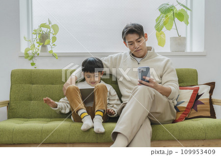 親子の日常　イメージ　スマートフォンを見る父親とタブレットを見る息子 109953409