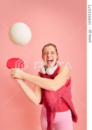 Dynamic portrait of young expressive lady hits ball with tennis racket in motion against pastel pink background. Concept of hobby, sport 109955075