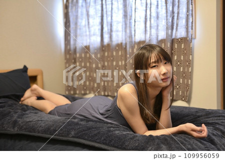ベッドの上でくつろぐワンピース姿の若い女性 109956059