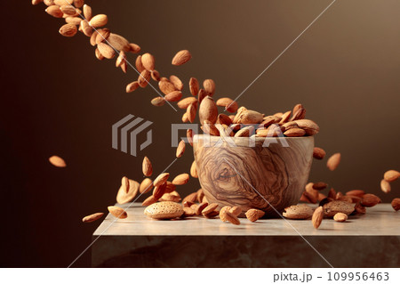 Almond nuts are poured into a wooden bowl. 109956463