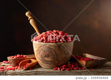 Dried goji berries in wooden bowl on a brown background. 109956469