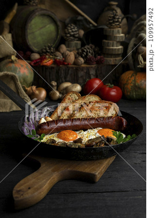Fried eggs and sausage with mushrooms served in cast iron pan in the kitchen Fried eggs and sausage with mushrooms served in cast iron pan in the kitchen 109957492