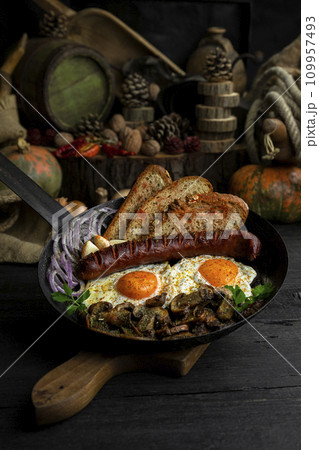 Fried eggs and sausage with mushrooms served in cast iron pan in the kitchen Fried eggs and sausage with mushrooms served in cast iron pan in the kitchen 109957493