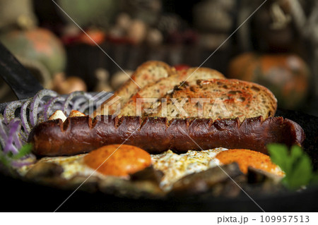 Sausage and fried eggs with toasted bread, mushrooms and onions served in cast iron dish. Selective focus on the sausage Sausage and fried eggs with toasted bread, mushrooms and onions served in cast iron dish. Selective focus on the sausage 109957513