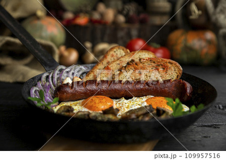Sausage and fried eggs with toasted bread, mushrooms and onions served in cast iron dish. Selective focus on the sausage Sausage and fried eggs with toasted bread, mushrooms and onions served in cast iron dish. Selective focus on the sausage 109957516