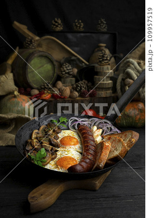 Fried eggs and sausage with mushrooms served in cast iron pan in the kitchen 109957519