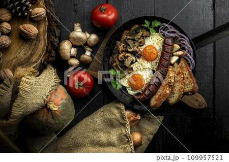 Fried eggs and sausage with mushrooms served in cast iron pan in the kitchen. Top view, flat lay 109957521