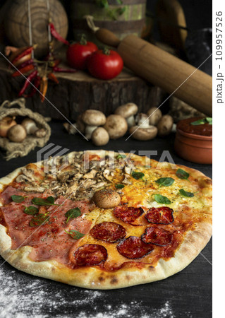 Italian Pizza Four Seasons (Pizza Quattro Stagioni) with different ingredients on the wooden table in the kitchen 109957526