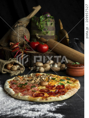 Italian Pizza Four Seasons (Pizza Quattro Stagioni) with different ingredients on the wooden table in the kitchen 109957527