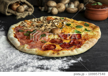 Italian Pizza Four Seasons (Pizza Quattro Stagioni) with different ingredients on the wooden table in the kitchen Italian Pizza Four Seasons (Pizza Quattro Stagioni) with different ingredients on the wooden table in the kitchen 109957540
