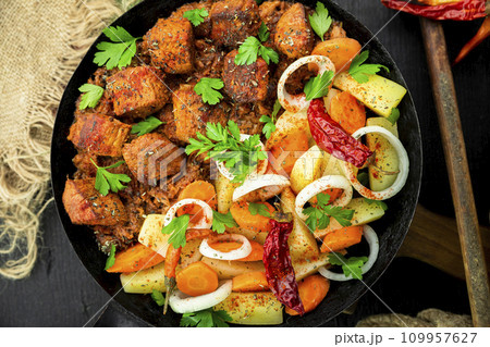 Stew with meat and vegetables in black iron dish. Traditional gourmet goulash in a rustic kitchen. Top view Stew with meat and vegetables in black iron dish. Traditional gourmet goulash in a rustic kitchen. Top view 109957627
