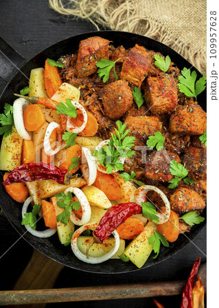 Stew with meat and vegetables in black iron dish. Traditional gourmet goulash in a rustic kitchen. Top view Stew with meat and vegetables in black iron dish. Traditional gourmet goulash in a rustic kitchen. Top view 109957628