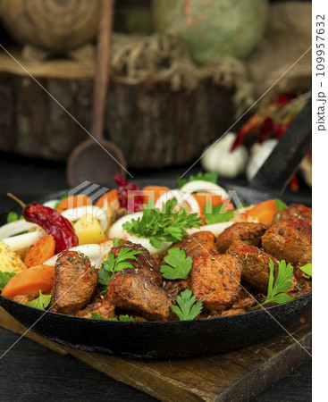 Stew with meat and vegetables in black iron dish. Traditional gourmet goulash in a rustic kitchen Stew with meat and vegetables in black iron dish. Traditional gourmet goulash in a rustic kitchen 109957632