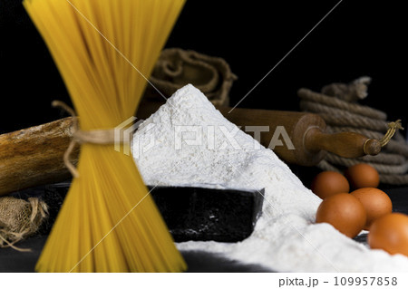 Pile of Flour with Spaghetti, eggs and vintage, rustic utensils in background. Selective focus on the Flour Pile of Flour with Spaghetti, eggs and vintage, rustic utensils in background. Selective focus on the Flour 109957858