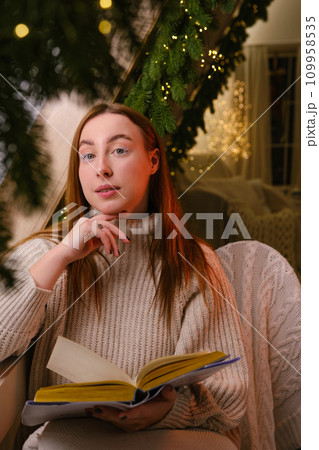 Hello winter. smiling modern woman in white sweater siting on chair and reading a book in room decorated for celebrating the new year and christmas festive mood Hello winter. smiling modern woman in white sweater siting on chair and reading a book in room decorated for celebrating the new year and christmas festive mood 109958535