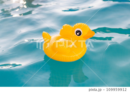Yellow inflatable duck floating on blue water in a pool on a hot summer day 109959912