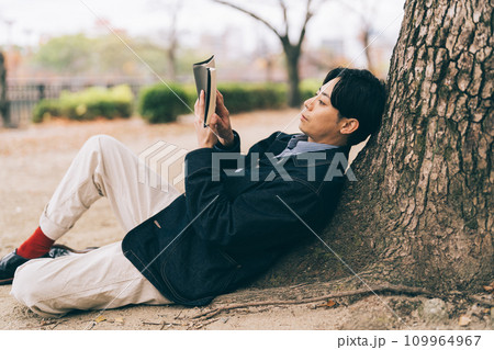 木にもたれて本を読む男性 109964967