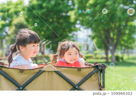 公園でキャリーカートに乗って遊ぶ姉妹の女の子（子供・幼児・少女） 109966302