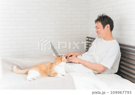 家の寝室・ベッドルームで猫・ペットと一緒にテレワーク・リモートワークする男性 家の寝室・ベッドルームで猫・ペットと一緒にテレワーク・リモートワークする男性 109967793