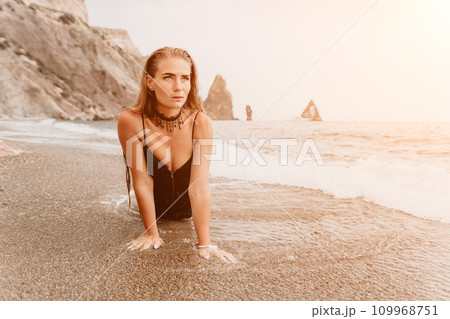 Woman summer travel sea. Happy tourist in black dress enjoy taking picture outdoors for memories. Woman traveler posing on sea beach surrounded by volcanic mountains, sharing travel adventure journey 109968751