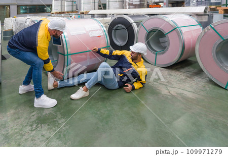 Two factory worker are carefully handling a large roll of steel, but one worker appear to have injured his leg. 109971279