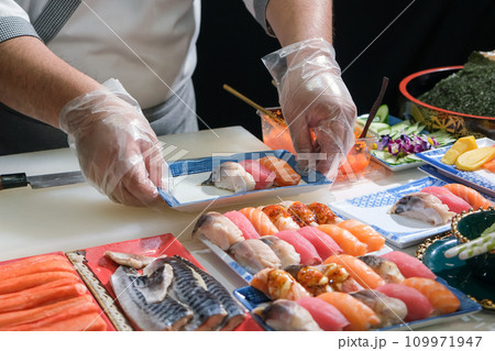 A skilled chef prepare a variety of sushi on a table. Mixing flavor, texture, and color, the chef creates culinary art. Each sushi is a precise masterpiece, showcasing their expertise and dedication. A skilled chef prepare a variety of sushi on a table. Mixing flavor, texture, and color, the chef creates culinary art. Each sushi is a precise masterpiece, showcasing their expertise and dedication. 109971947