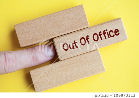 Finger pushing out wooden block with out of office text on yellow cover background. Finger pushing out wooden block with out of office text on yellow cover background. 109973312