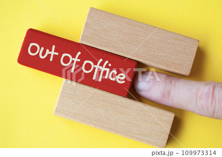 Finger pushing out red wooden block with out of office text on yellow cover background. 109973314