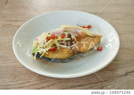 deep fried Indo-Pacific king mackerel fish dressing slice mango with shallot couple chop chili sweet vinegar and fish sauce on plate 109975240