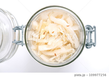 German sauerkraut, in an opened swing top glass jar. Cut raw cabbage, fermented by lactic acid bacteria. Traditionally a warm served side dish, flavored with juniper berries and caraway seeds. Photo. 109977256