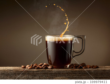 Espresso coffee glass cup with splashes on a brown background. Espresso coffee glass cup with splashes on a brown background. 109979411