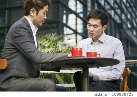 two asian corporate businesspeople discussing business at a outdoor coffee shop two asian corporate businesspeople discussing business at a outdoor coffee shop 109980728