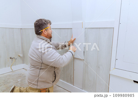 During installation of wooden trim moldings in room contractor nails wood with nails using air gun 109980985