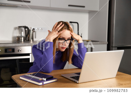 Annoyed young adult woman in glasses work study at kitchen using laptop. Remote education 109982783