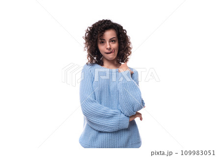 a young caucasian woman with curly dark hair is dressed in a casual warm blue sweater 109983051