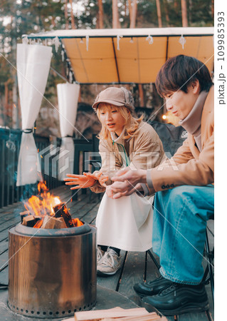 キャンプ場で焚き火をしているカップル 109985393