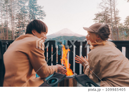 キャンプ場で焚き火をしているカップル 109985405