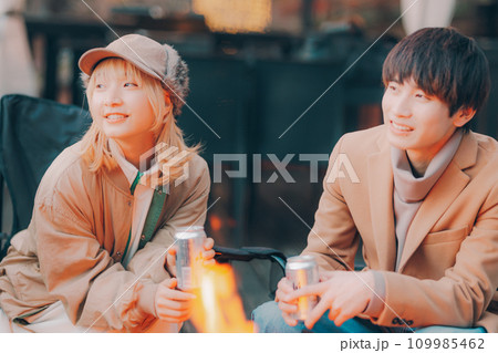 キャンプ場で焚き火をして乾杯をしているカップル 109985462
