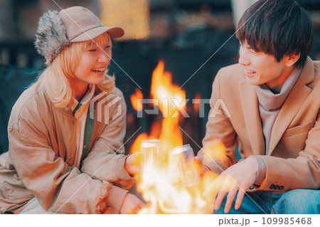 キャンプ場で焚き火をして乾杯をしているカップル 109985468
