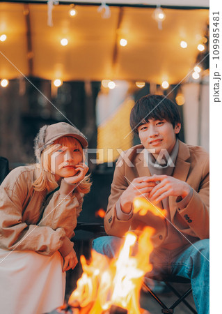 キャンプ場で焚き火をして乾杯をしているカップル 109985481
