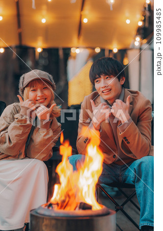 キャンプ場で焚き火をして乾杯をしているカップル 109985485