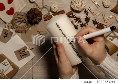 Unrecognizable young woman paint numbers on candles. Female making homemade advent calendar Made with your own hands step by step DIY crafts do it yourself. Preparation to christmas concept. Seasonal 109985694