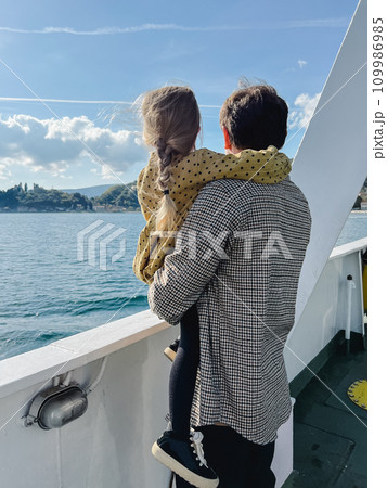 Dad with a little girl in his arms stands on board a boat floating on the sea and looks at the shore Dad with a little girl in his arms stands on board a boat floating on the sea and looks at the shore 109986985