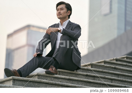 outdoor portrait of a successful asian business man sitting on steps in full suit outdoor portrait of a successful asian business man sitting on steps in full suit 109989468