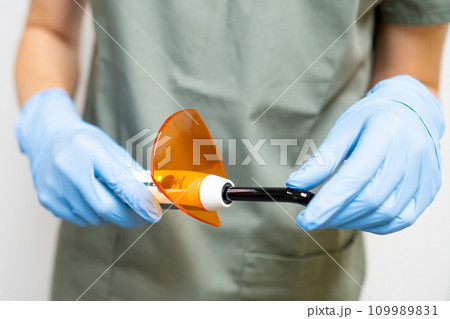 Dental ultraviolet curing light tool with orange UV light blocking glass in dentist hands. 109989831
